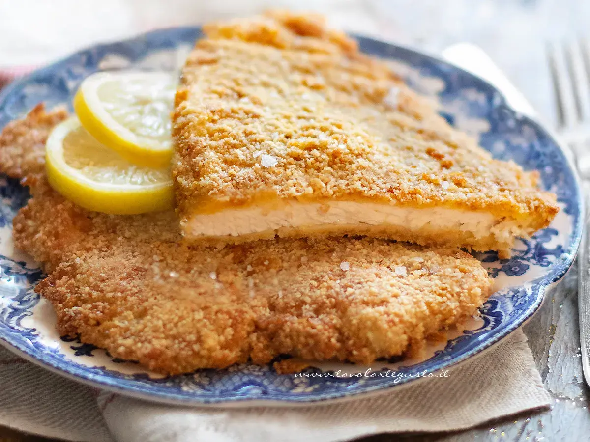 Due cotolette al forno dorate e croccanti, servite su un piatto blu con spicchi di limone.
