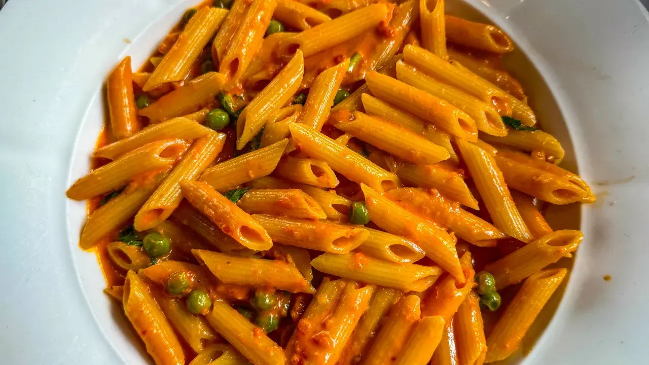 Penne ai 7 peccati, un piatto di pasta avvolto in una cremosa salsa rossa, con piselli verdi che spuntano come gemme preziose.