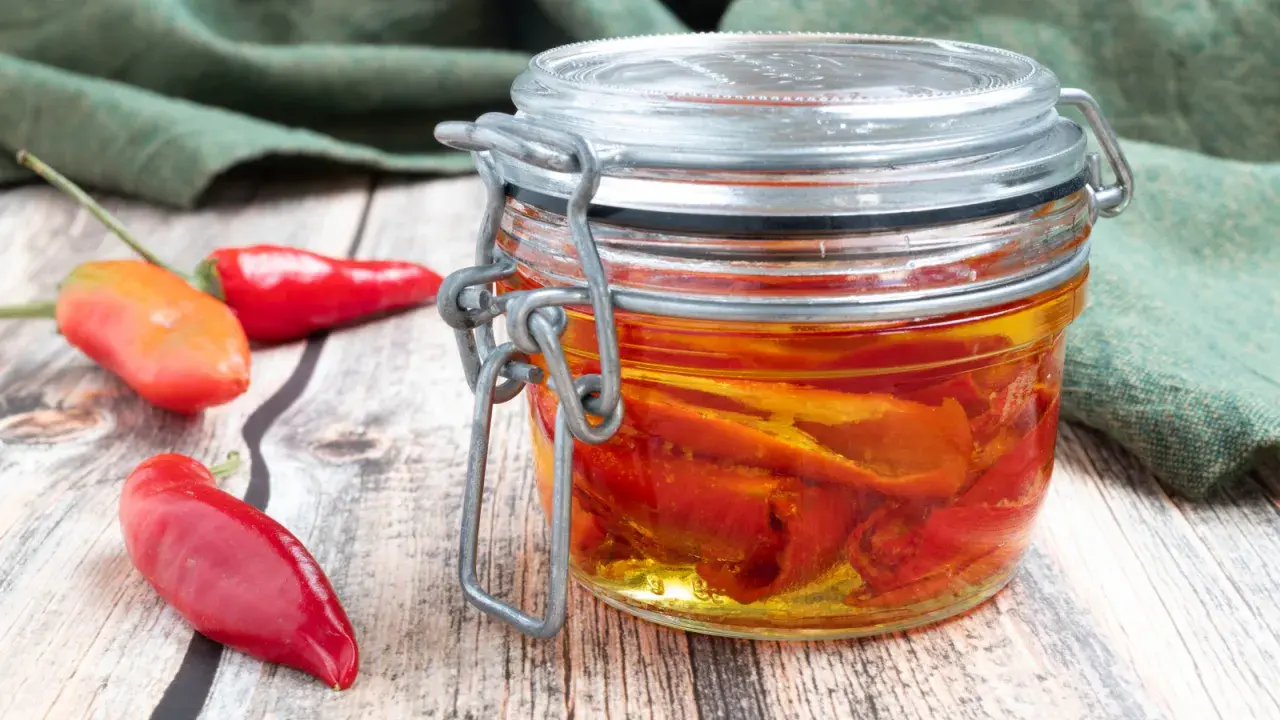 Barattolo di **olio al peperoncino** fatto in casa, con peperoncini rossi freschi accanto su un tavolo di legno.