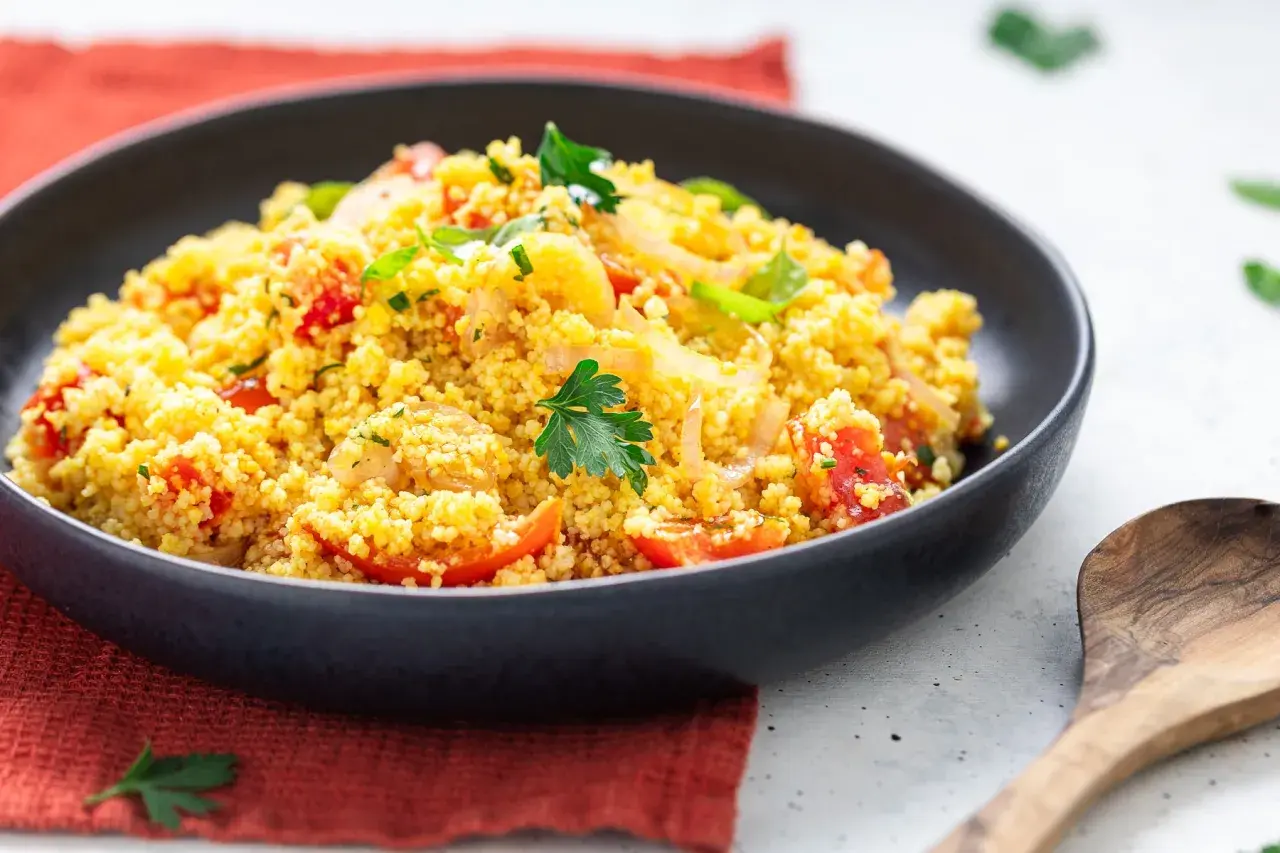 Un piatto invitante di cous cous freddo con pomodorini, cipolle e prezzemolo fresco. Perfetto per un pasto leggero e saporito.