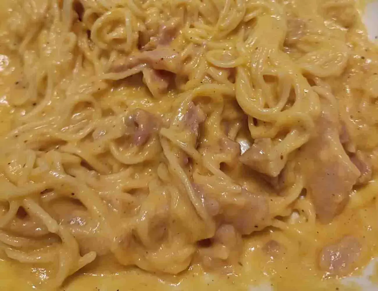 Un piatto cremoso di pasta alla carbonara, con spaghetti avvolti in una salsa dorata e pezzetti di guanciale.