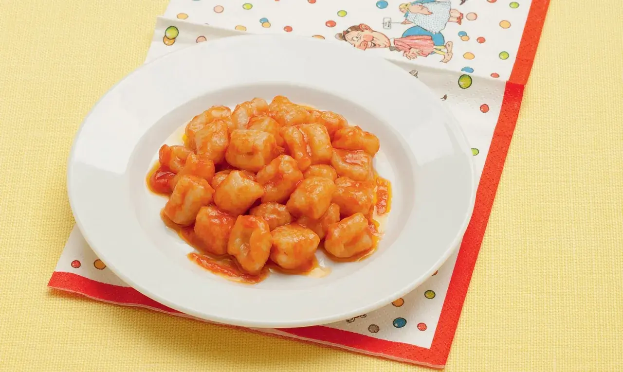 Un piatto di chicche di patate condite con un sugo rosso, servite su un tovagliolo colorato.
