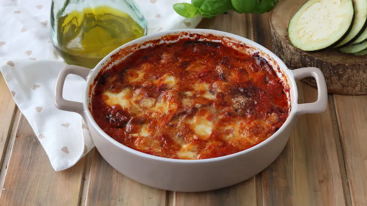 Parmigiana di melanzane appena sfornata, dorata e filante, con pomodoro e basilico fresco.