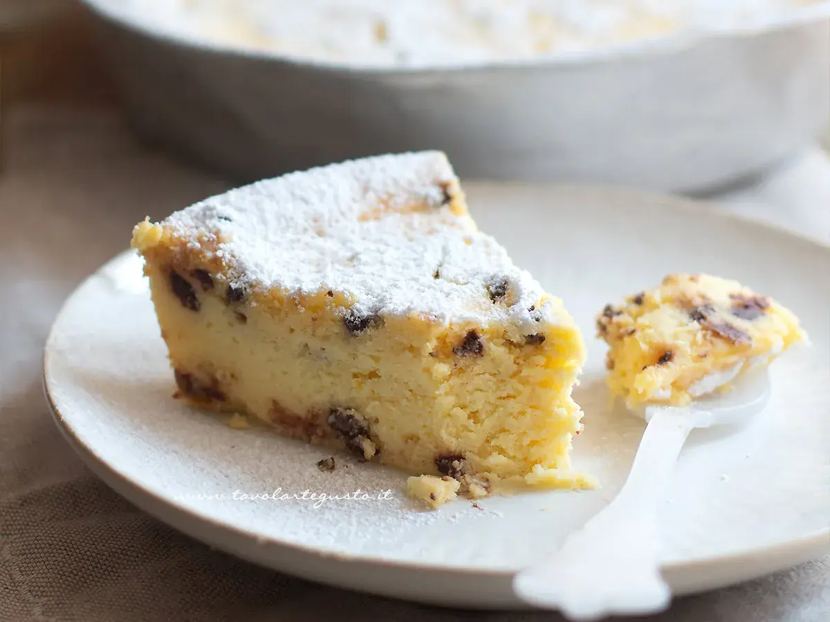 Una fetta di torta ricotta veloce, soffice e cosparsa di zucchero a velo, con gocce di cioccolato. Un assaggio delizioso.