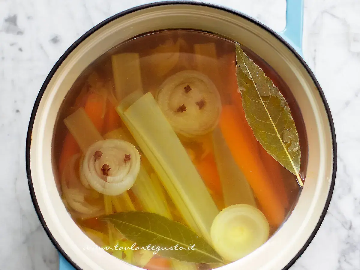 Brodo vegetale ricetta: carote, sedano, cipolla con chiodi di garofano e alloro in pentola.
