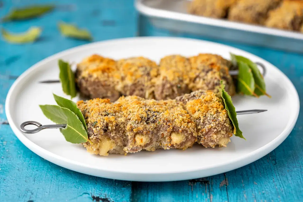 Braciole alla messinese su spiedini, impanate e dorate, guarnite con foglie di alloro.