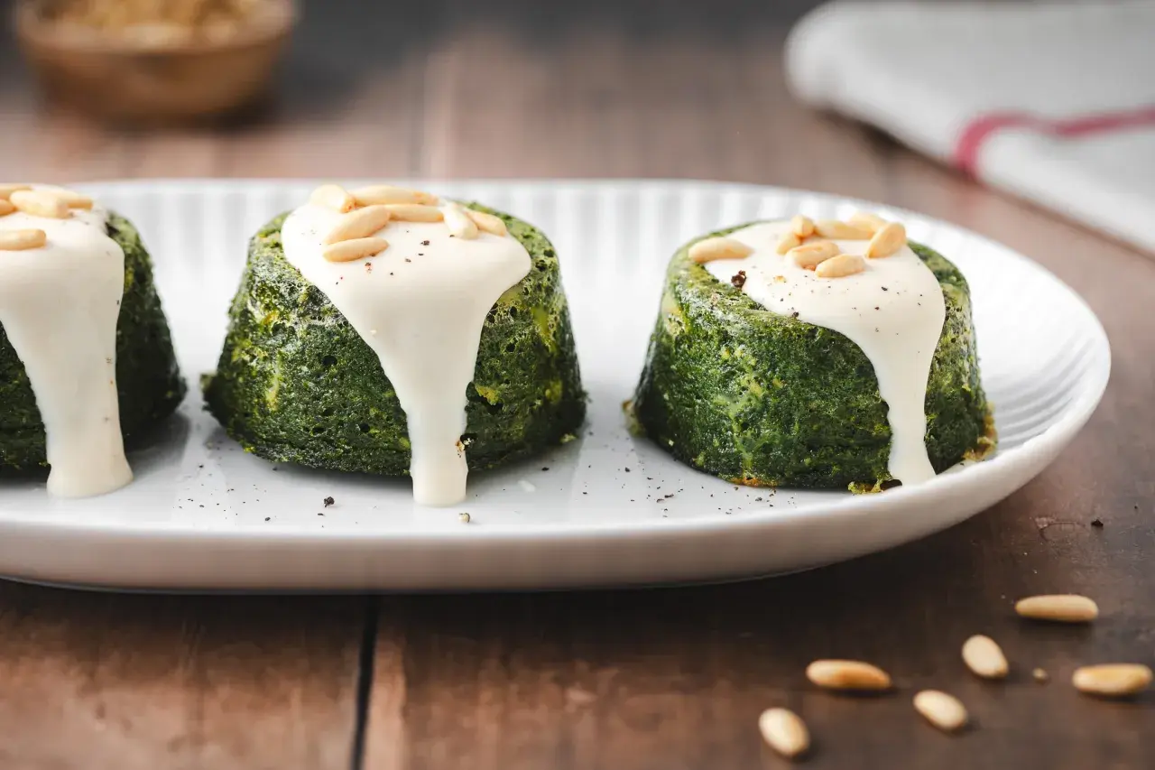 Delizioso flan di verdure servito su un piatto bianco, guarnito con salsa cremosa e pinoli tostati.
