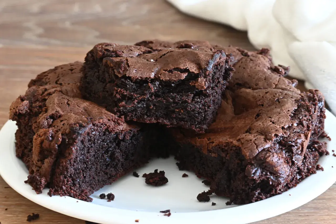 Torta al cioccolato, soffice e umida, tagliata a fette su un piatto bianco. La crosta è leggermente screpolata, rivelando l'interno scuro e invitante.