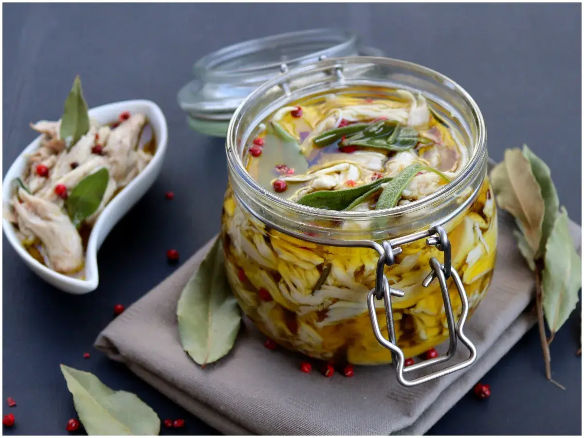 Tonno di coniglio sott'olio, sfilacciato e conservato in un barattolo di vetro con erbe aromatiche e pepe rosa.
