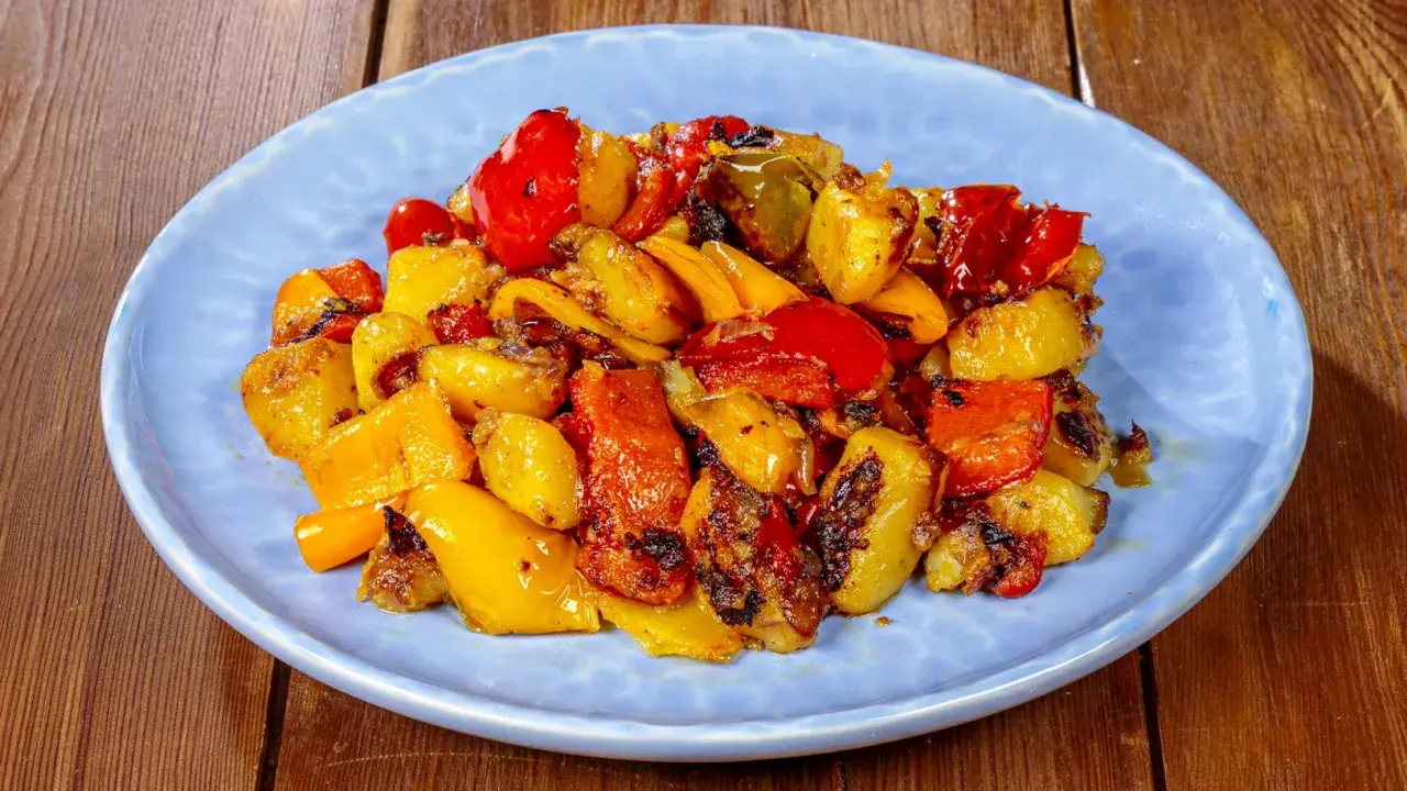 Pipi e patate arrostiti, un contorno colorato e saporito, servito su un piatto azzurro.