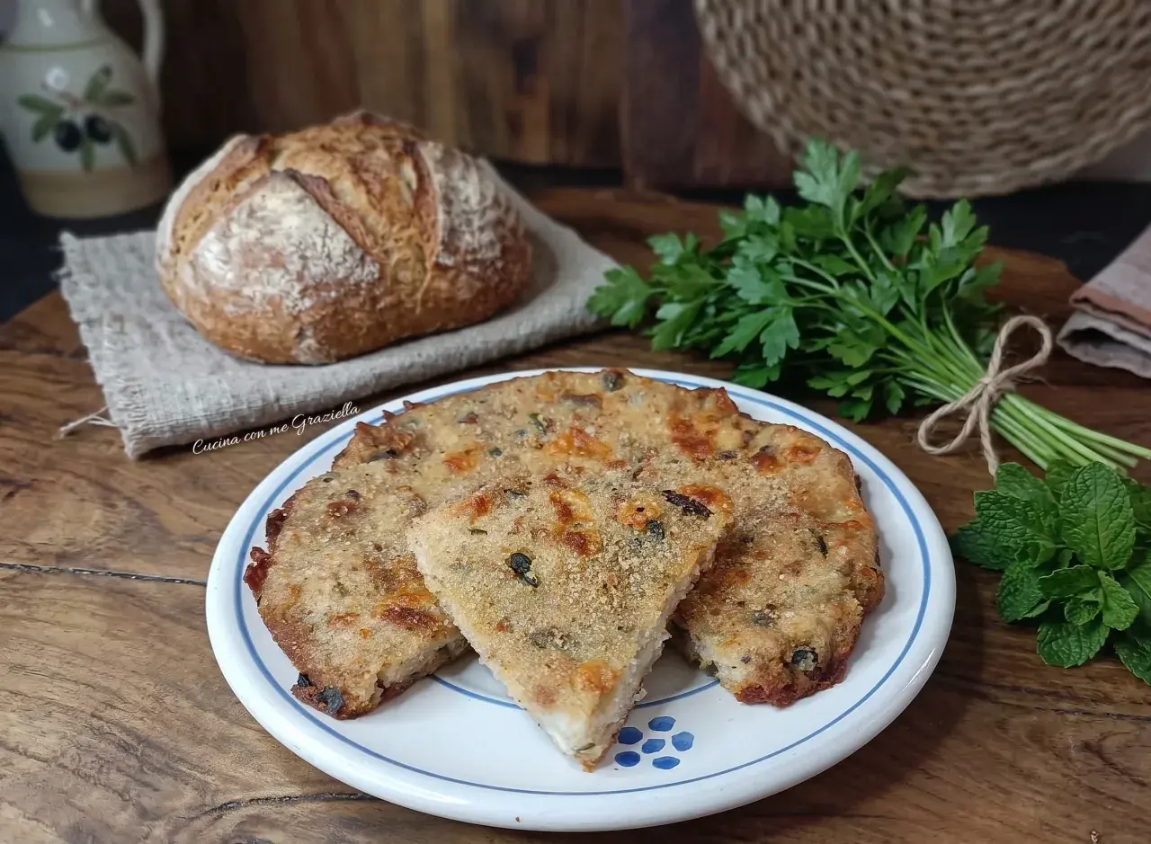 Frittata di pane dorata e saporita, servita su un piatto bianco con bordi blu, accanto a pane fresco e erbe aromatiche.
