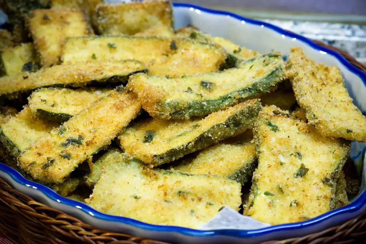 Fettine di zucchine impanate e dorate, appena tolte dalla padella, servite in una ciotola.