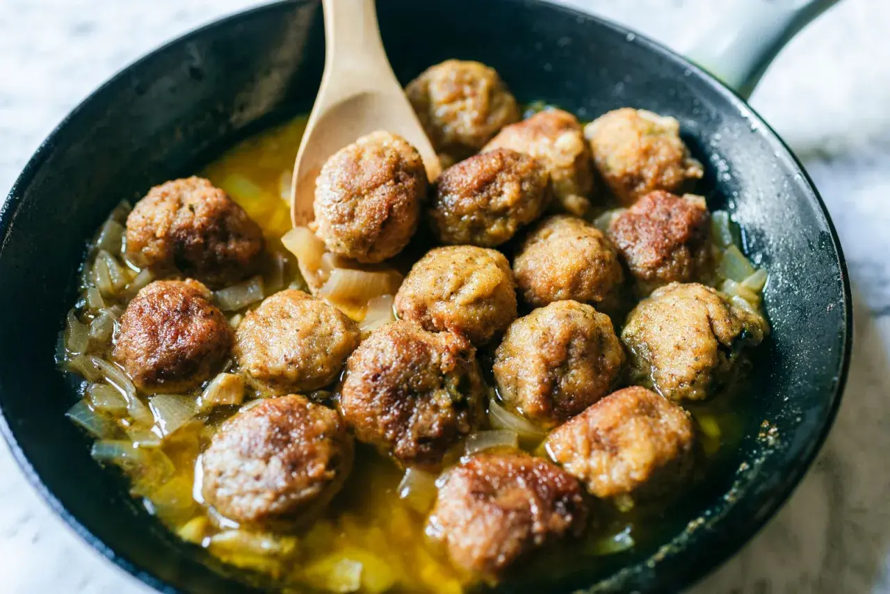Polpette in bianco succulente in padella con cipolle caramellate, pronte per essere gustate.