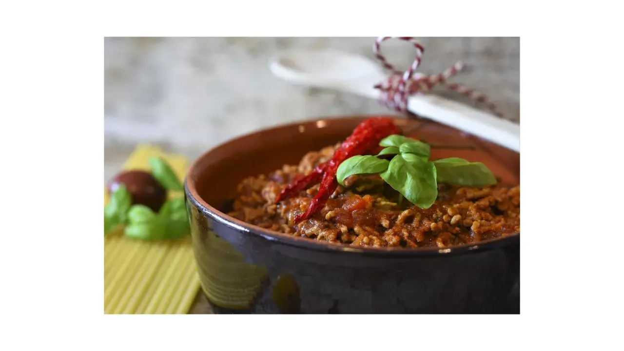 Un saporito ragù di verdure, guarnito con peperoncino e basilico, in una ciotola di terracotta.