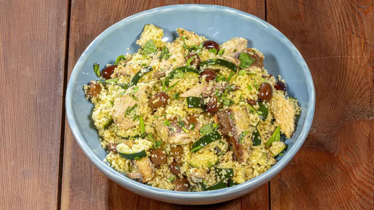 Un saporito cous cous con verdure, olive e pesce, guarnito con erbe fresche.
