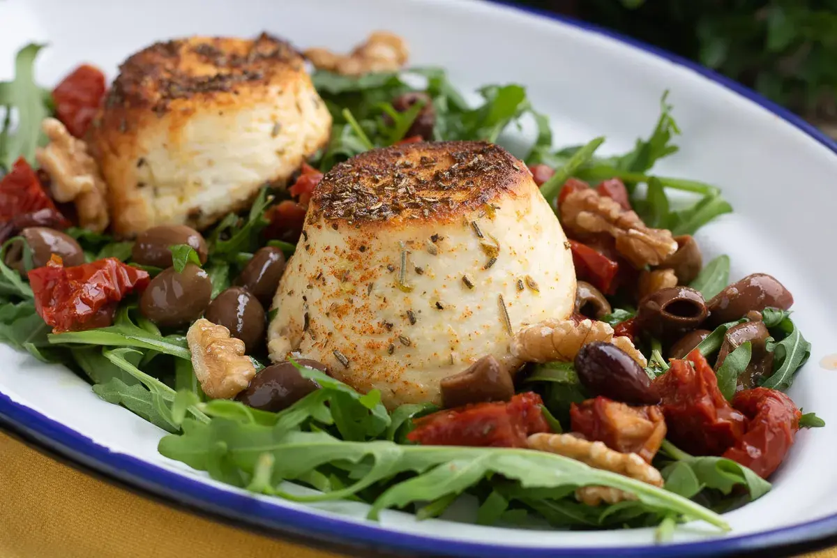 Due dischi di ricotta al forno su un letto di rucola, pomodori secchi, olive e noci.