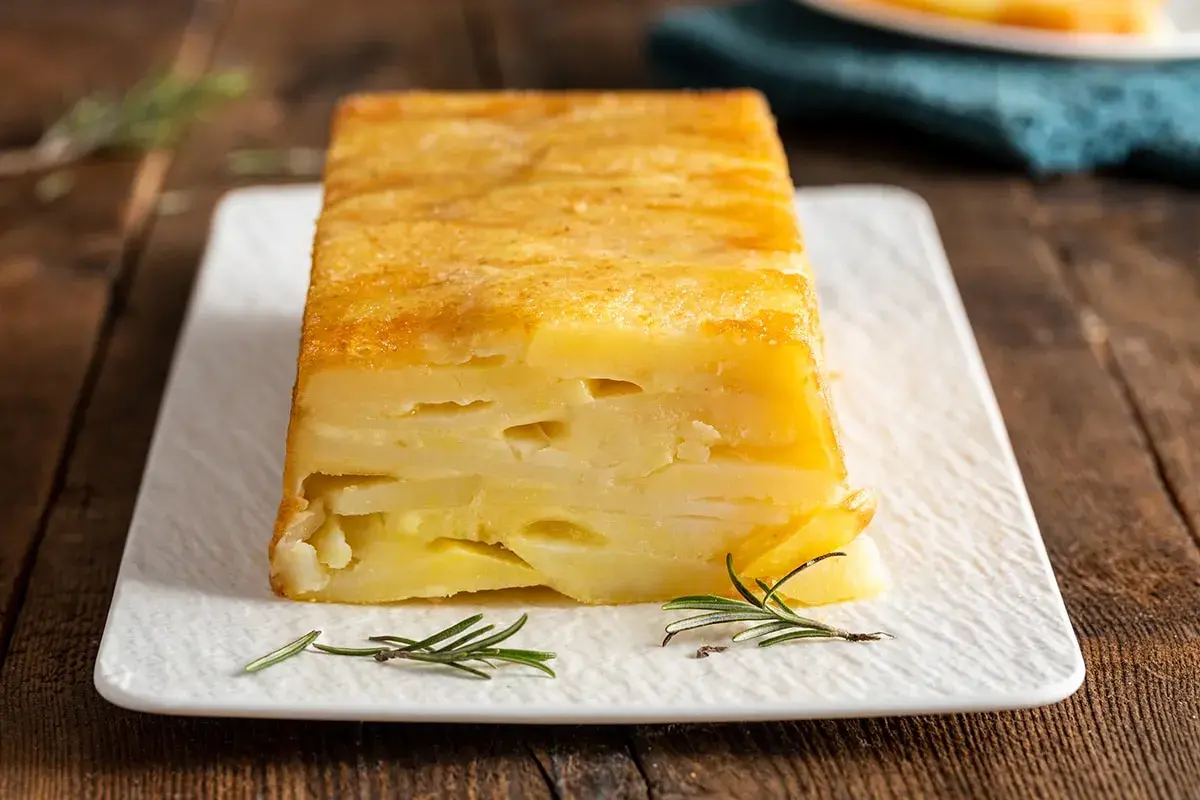 Sformato di patate a fette dorato e invitante, servito su un piatto bianco con rametti di rosmarino.