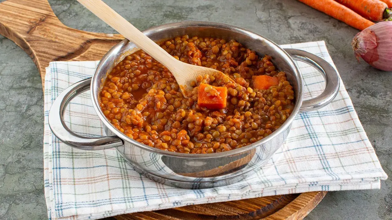 Un pentolino pieno di saporito ragù di lenticchie, con pezzi di carota e un cucchiaio di legno.