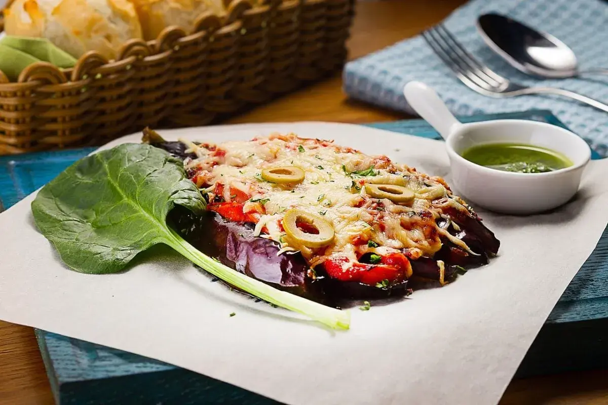 Caponata di melanzane gratinata con olive, pomodoro e formaggio fuso, servita con spinaci freschi e salsa verde.