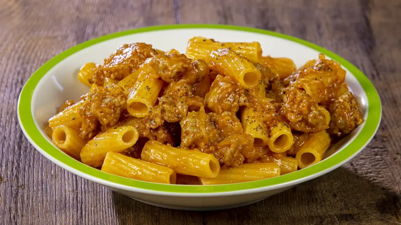 Piatto di rigatoni conditi con un ricco sugo di salsiccia, cosparso di pepe nero.