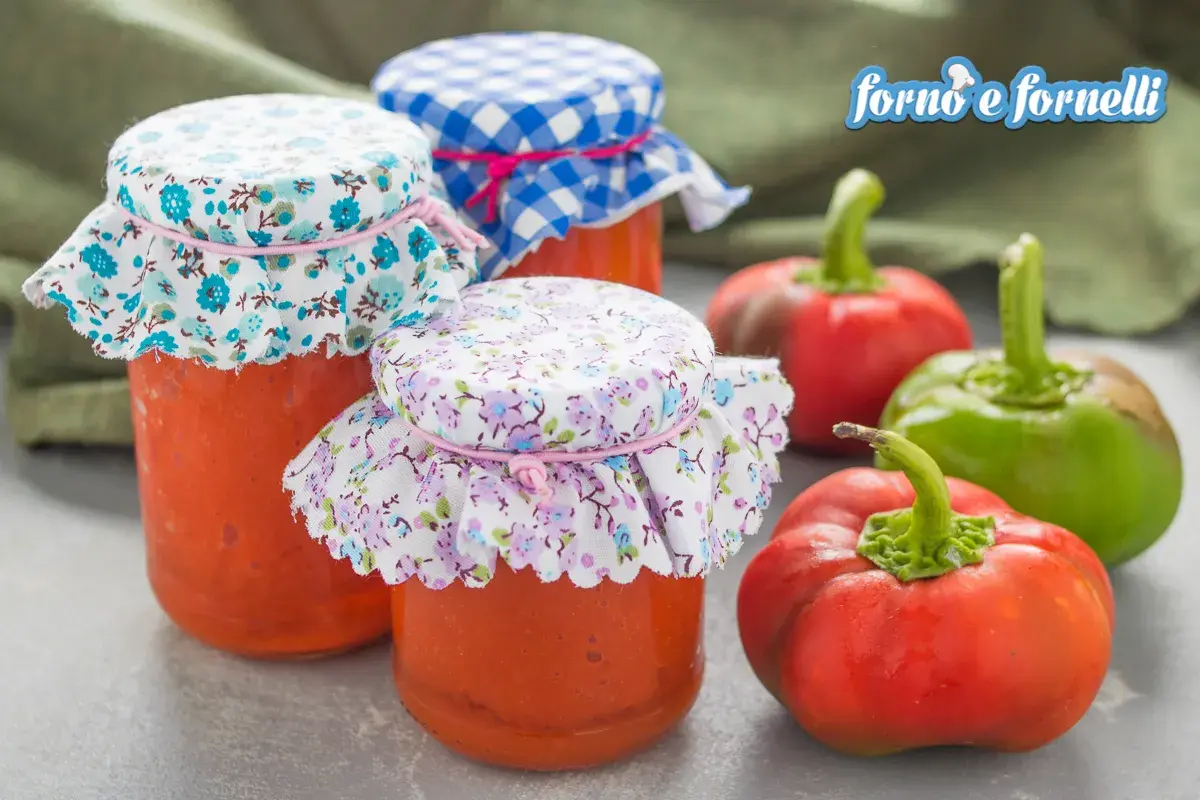 Barattoli di crema di peperoni fatti in casa, decorati con stoffe floreali e a quadretti, accanto a peperoni freschi.