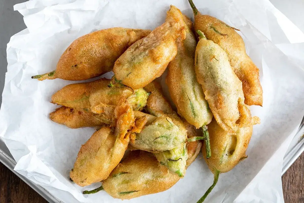 Un mucchio di fiori di zucca dorati e croccanti, impanati e fritti, adagiati su carta bianca.