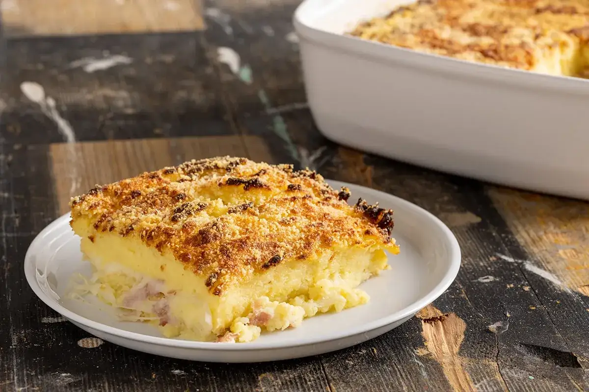 Una fetta di sformato di patate a fette dorato e croccante, con prosciutto e formaggio filante.