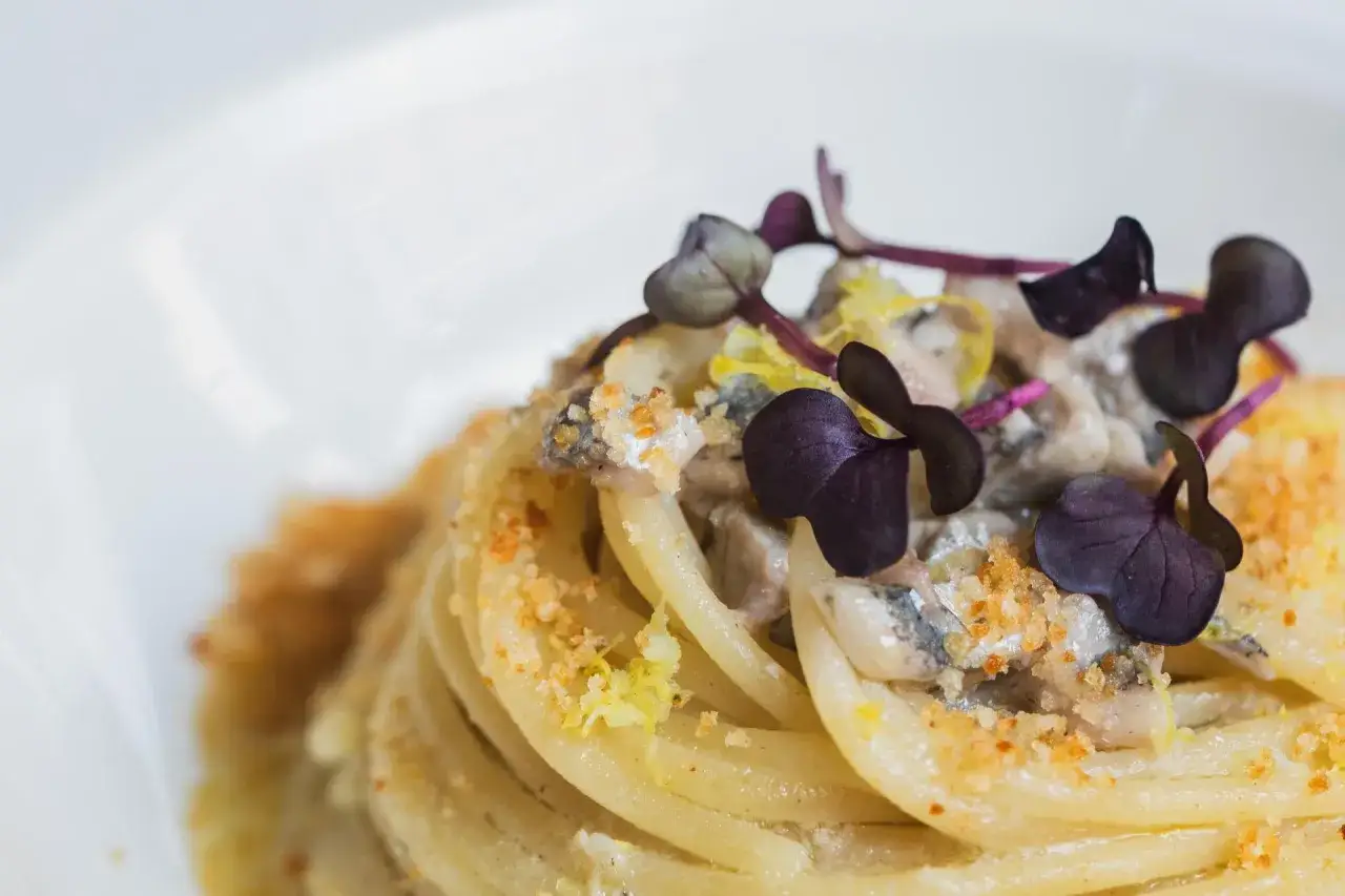 Spaghetti con burro e alici, guarniti con germogli viola e scorza di limone. Un piatto semplice ma gustoso.