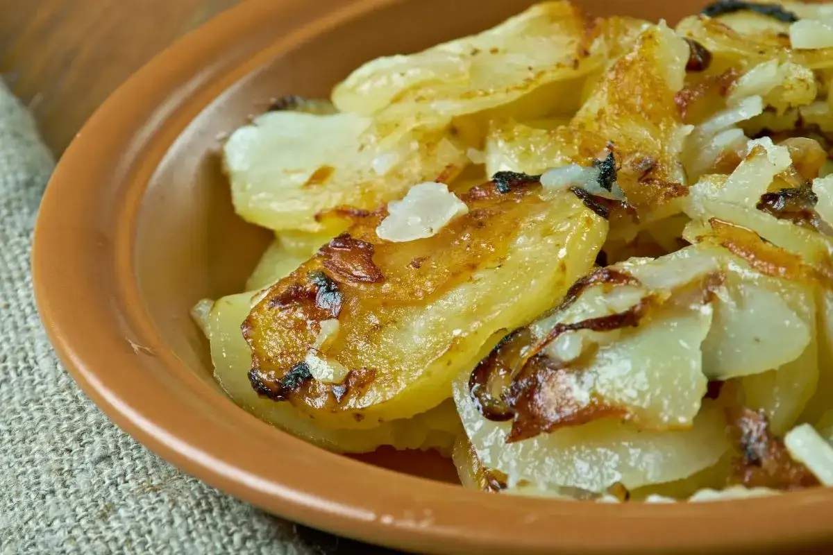Patate alla lionese dorate e croccanti, servite in una ciotola di terracotta. Un classico saporito.