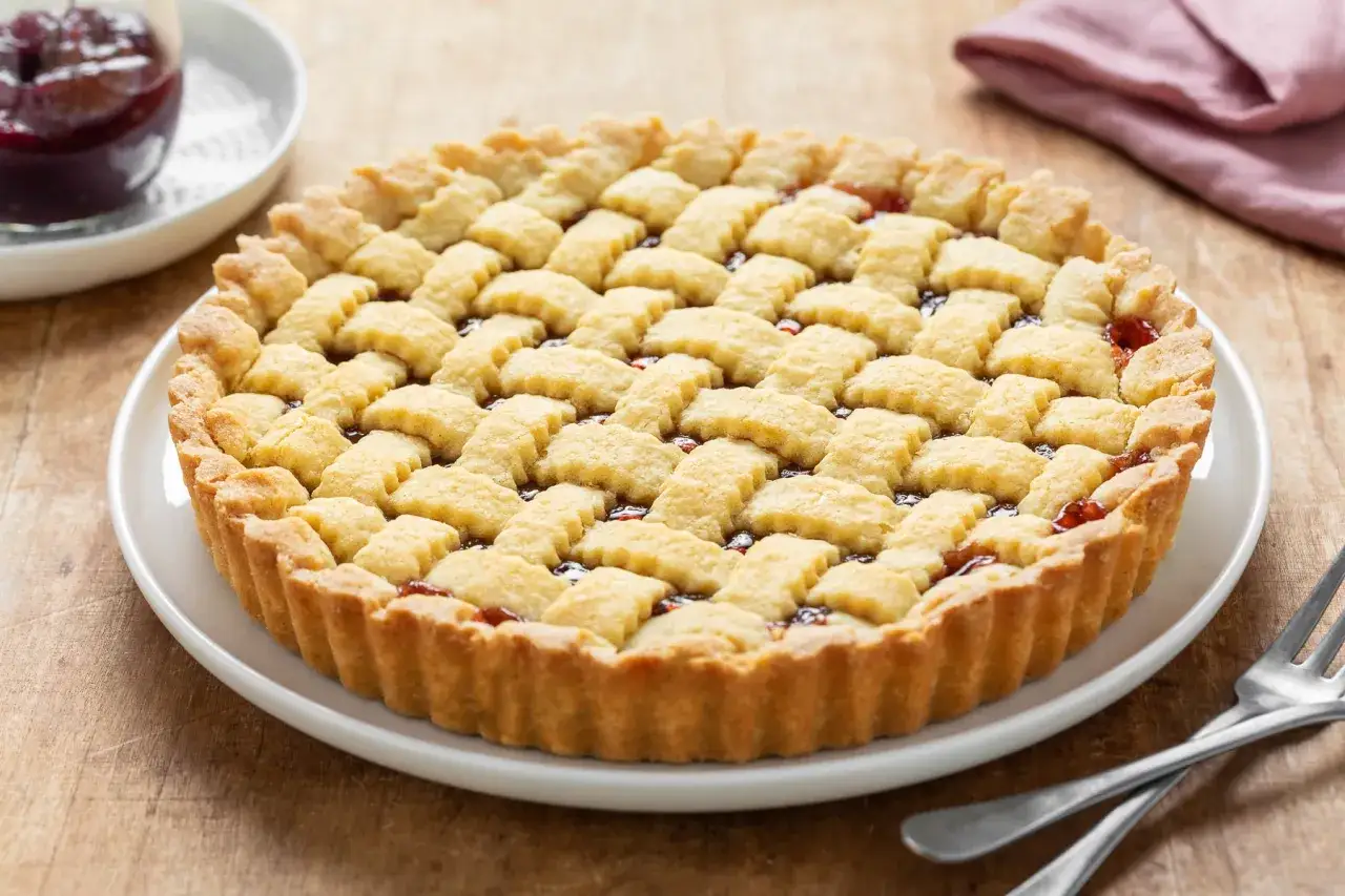Crostata con pasta frolla friabile per crostata, ripiena di marmellata di ciliegie, con decorazione a griglia.