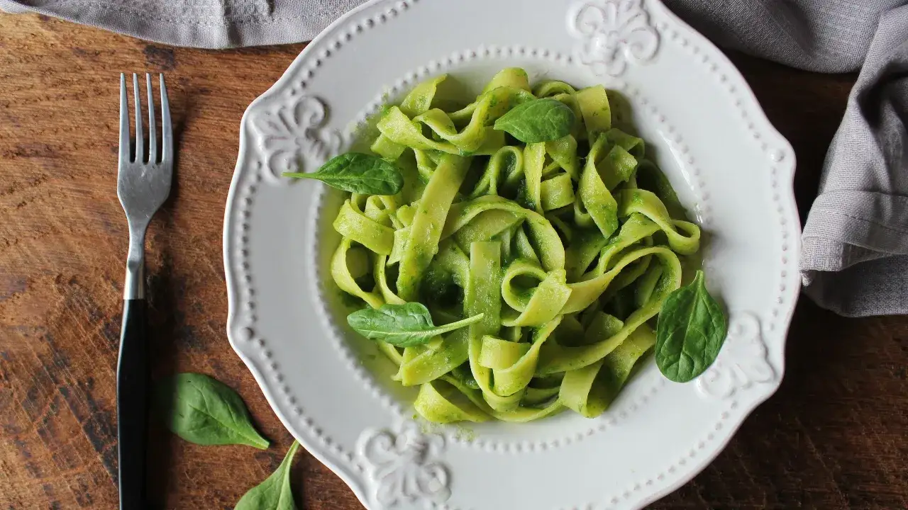 Un piatto di pasta veloce e sfiziosa, condita con un pesto verde brillante e foglie fresche di spinaci.