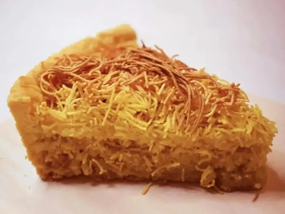 Una fetta di torta di tagliatelle, con la crosta dorata e un ripieno soffice, guarnita con fili croccanti.