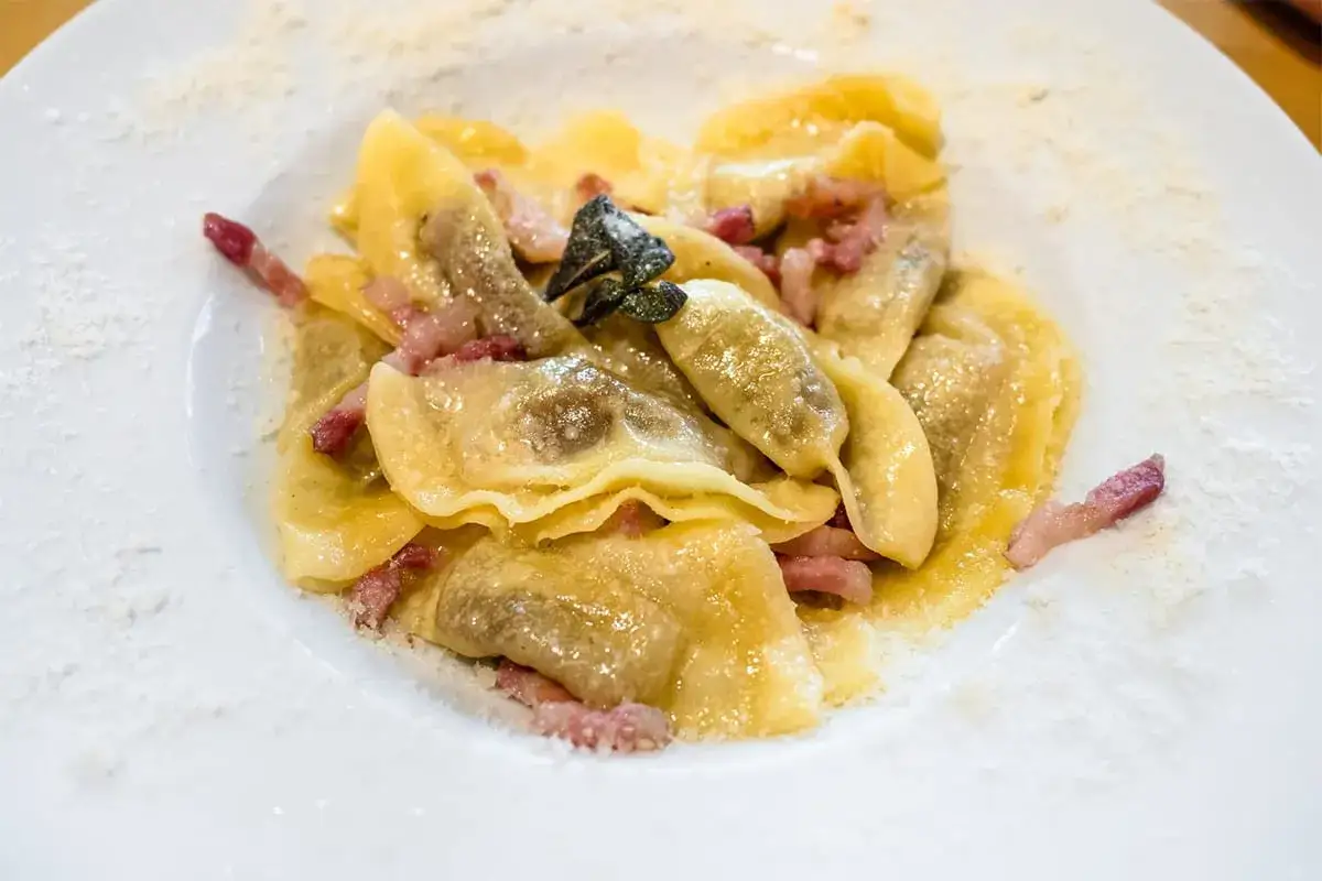 Piatto di casoncelli alla bergamasca conditi con burro, salvia e pancetta croccante, spolverati di formaggio grattugiato.