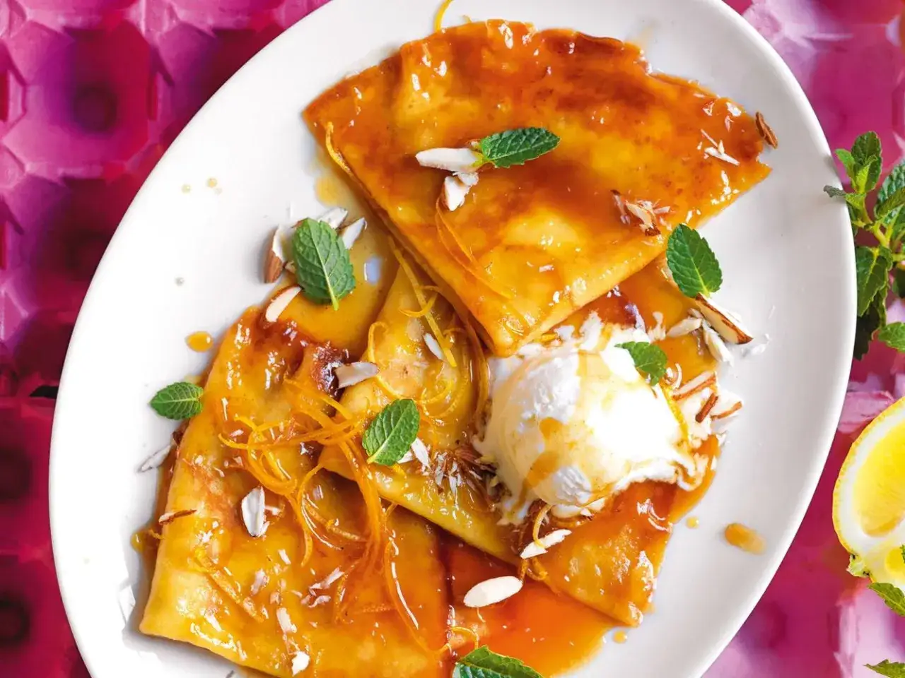 Deliziose crepes dolci con salsa all'arancia, gelato alla vaniglia, mandorle a lamelle e menta fresca. Una ricetta perfetta per un dessert goloso.
