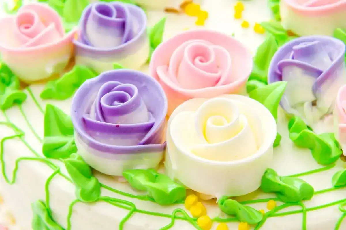 Torta decorata con rose colorate di pasta di zucchero, foglie verdi e gocce gialle.