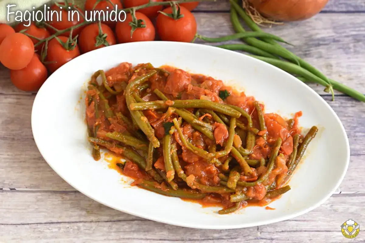 Fagiolini in umido, un piatto saporito con fagiolini verdi cotti in un sugo di pomodoro e cipolla, accompagnato da pomodorini freschi.