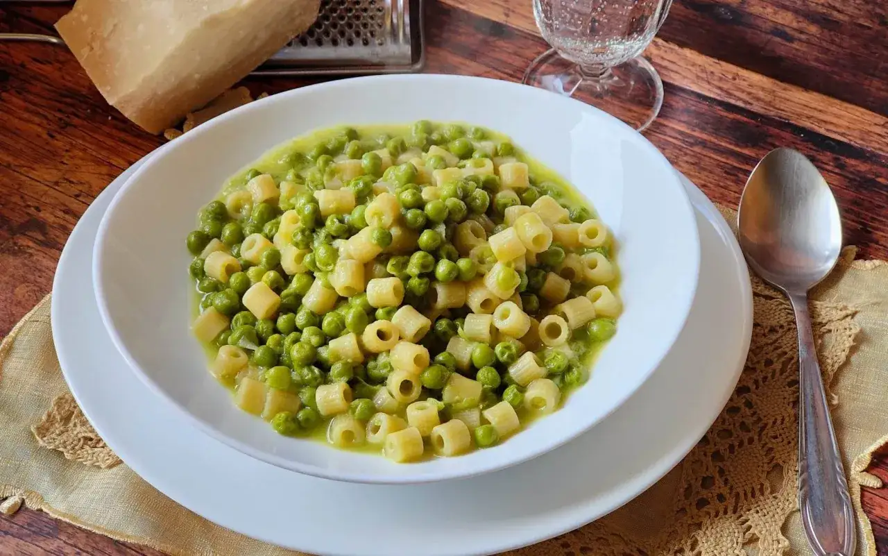 Un piatto di pasta e piselli cremoso, con un pezzo di parmigiano e una grattugia sullo sfondo.