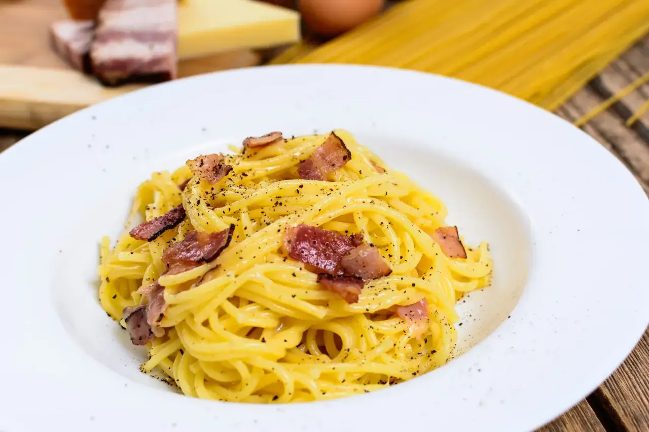 Un piatto di spaghetti alla carbonara fumante, conditi con guanciale croccante e pepe nero macinato fresco.