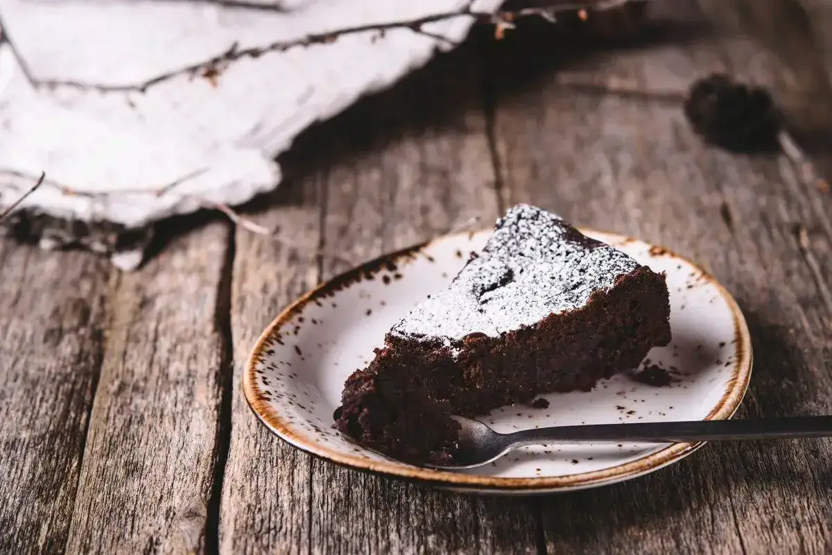 Una fetta di torta di pane al cioccolato, spolverata di zucchero a velo, su un piatto rustico con un cucchiaino.