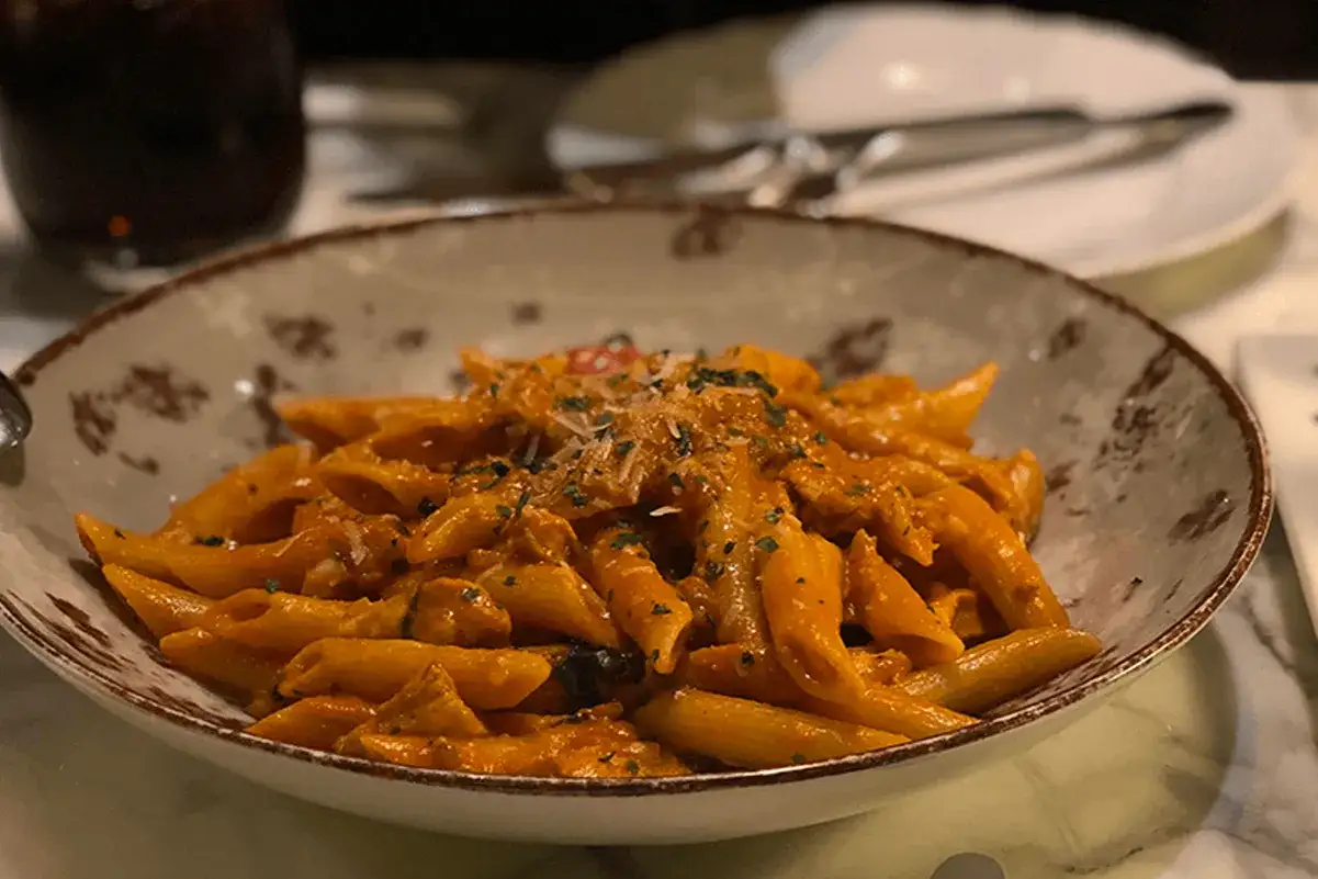 Penne al sugo rosso con melanzane, un classico piatto di pasta e melanzane alla napoletana, guarnito con parmigiano e prezzemolo.