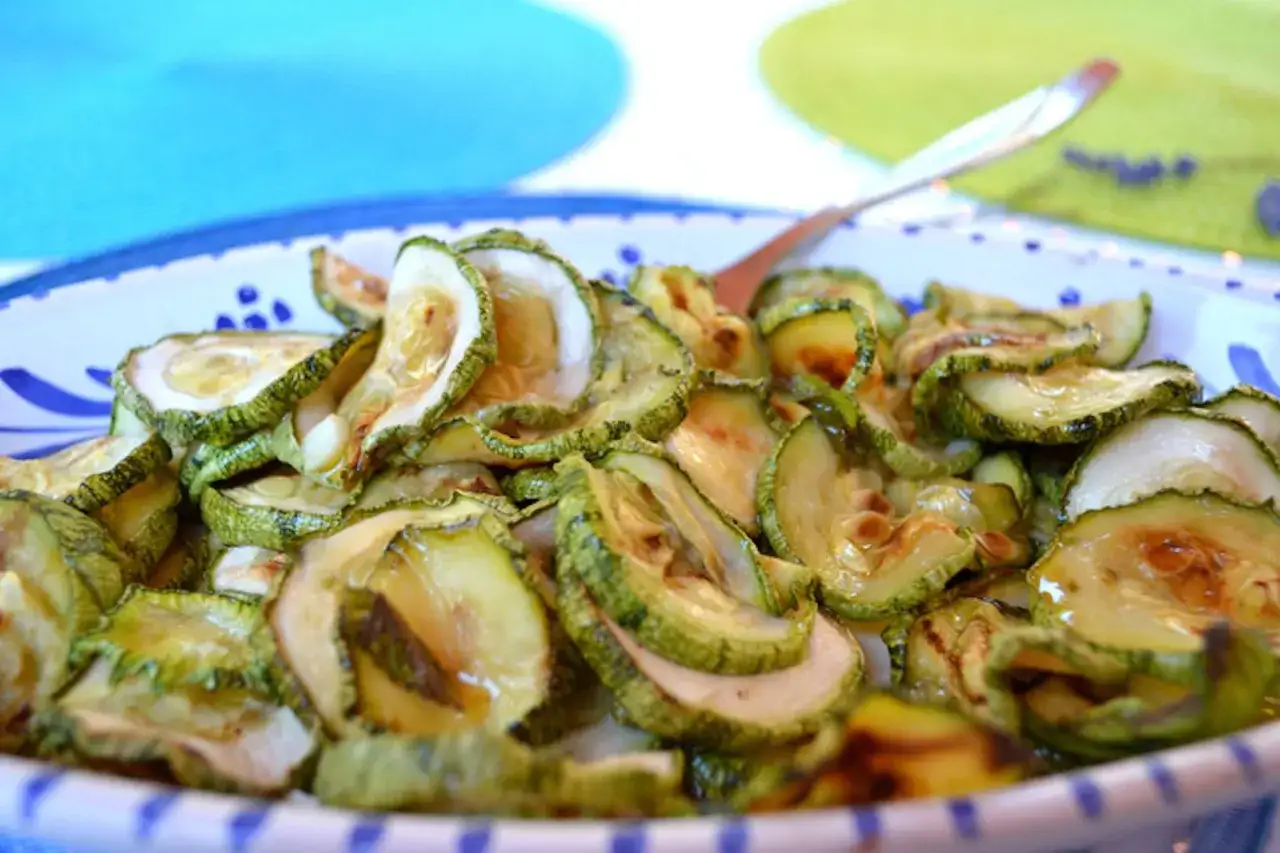 Fette di zucchine in carpione, condite con olio e aceto, servite in un piatto bianco con decorazioni blu.