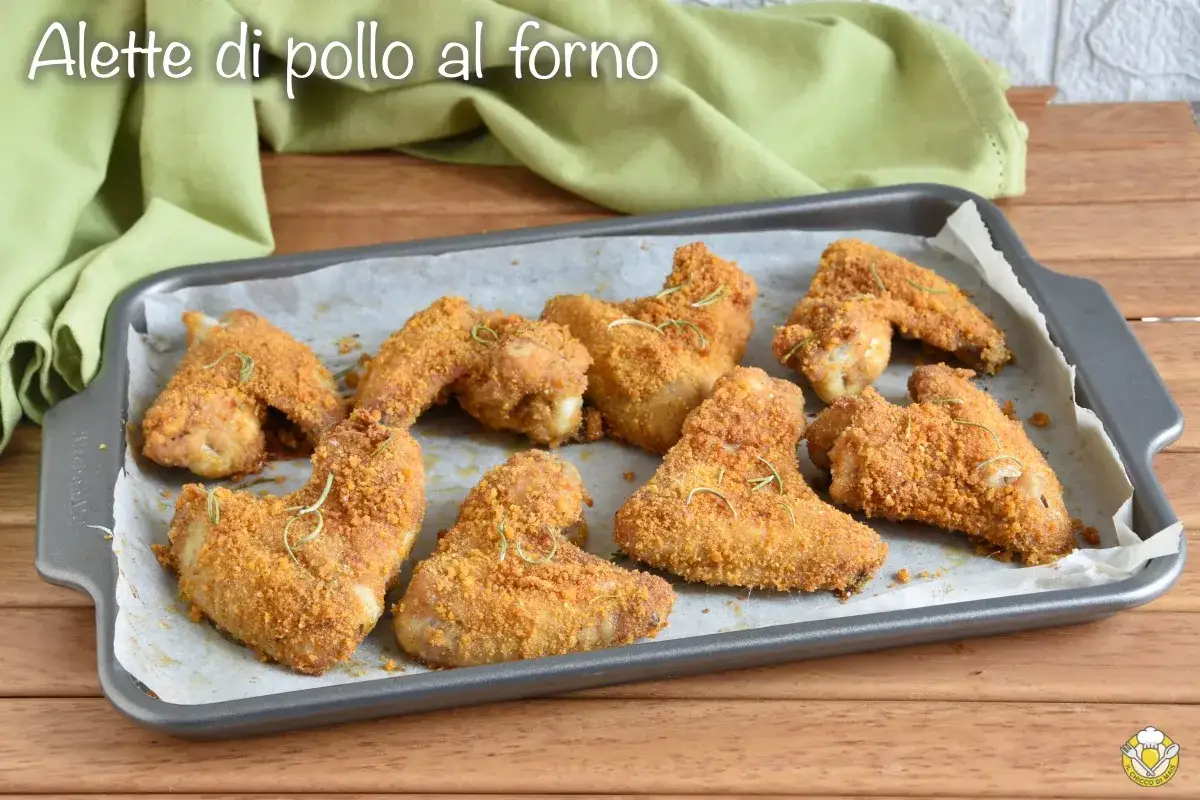 Alette di pollo al forno, dorate e croccanti, adagiate su una teglia con carta forno, guarnite con rosmarino.