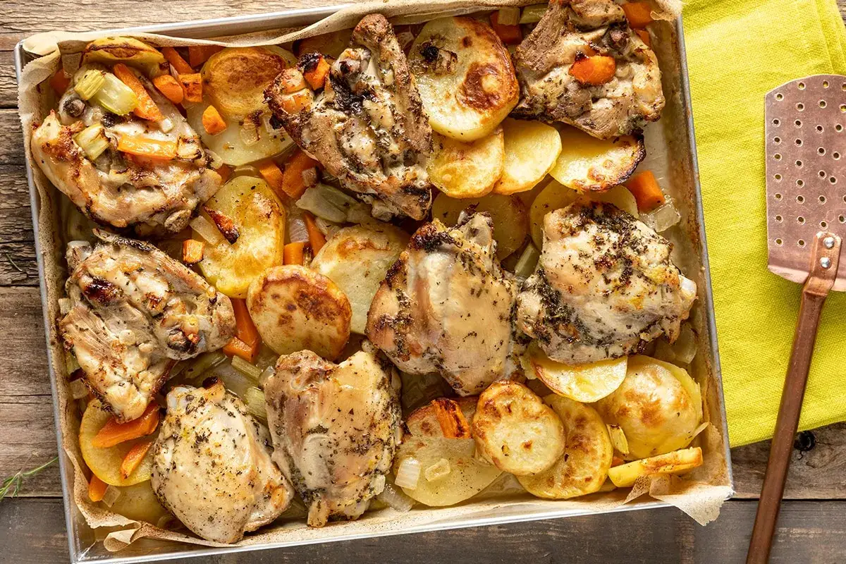 Sovracosce di pollo al forno dorate e succulente, adagiate su patate arrosto, carote e sedano in una teglia.