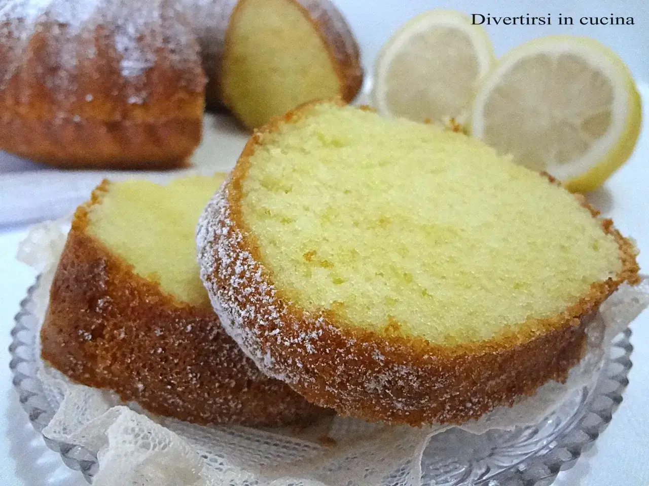 Fette di ciambellone al limone spolverate di zucchero a velo, con fette di limone sullo sfondo.
