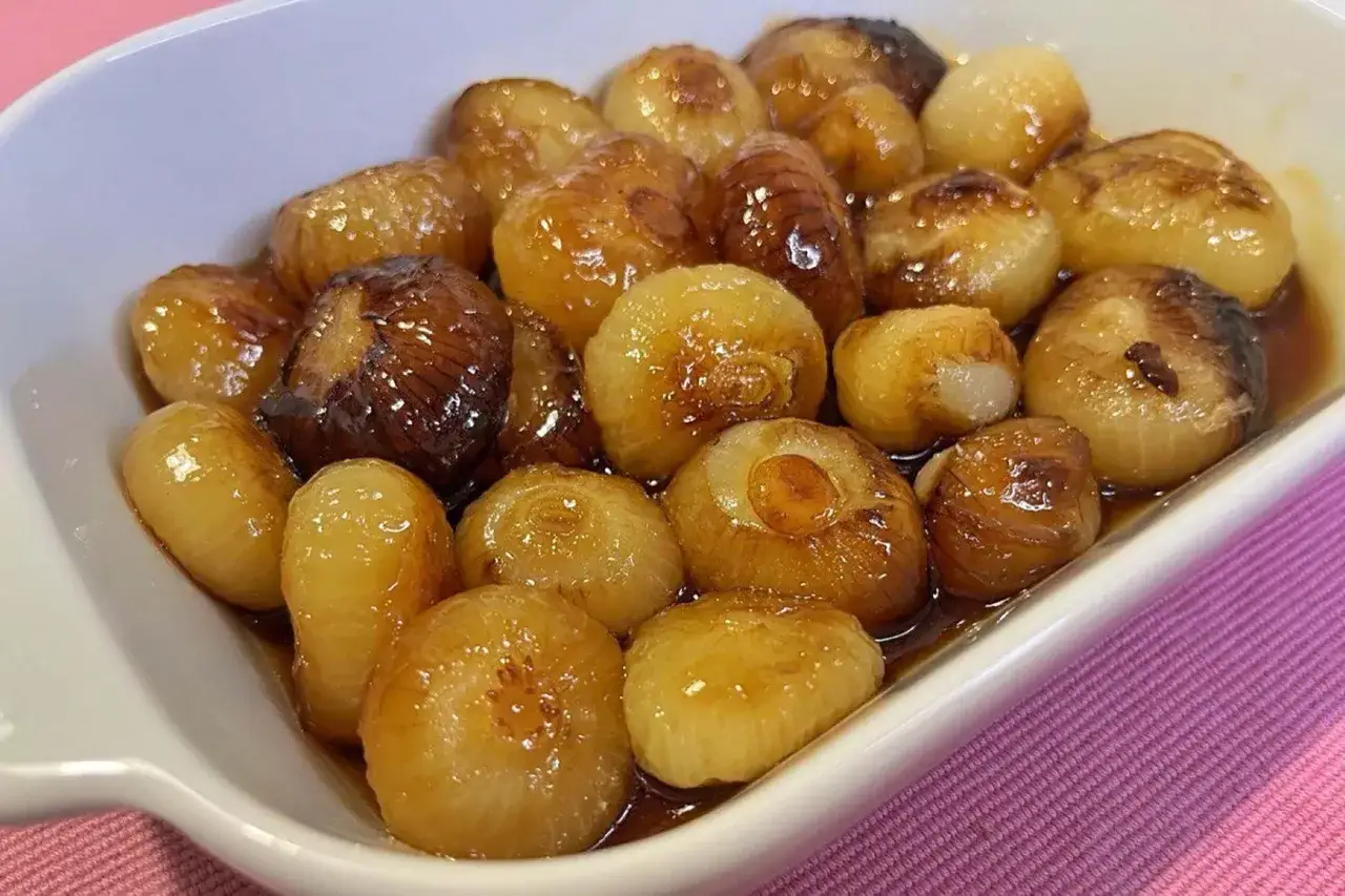 Cipolle in agrodolce caramellate, lucide e invitanti, servite in una ciotola bianca su un tovagliolo rosa.