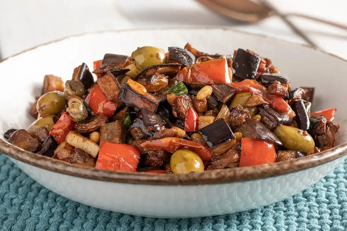 Un piatto invitante di caponata di melanzane, con melanzane a cubetti, peperoni rossi, olive verdi e capperi, condita con una salsa agrodolce.