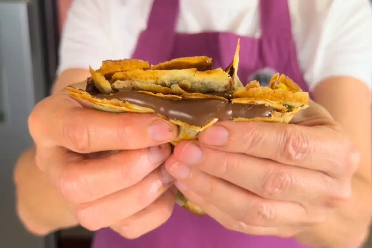 Mani che stringono una crepe ripiena di golosa Nutella, un piacere irresistibile.