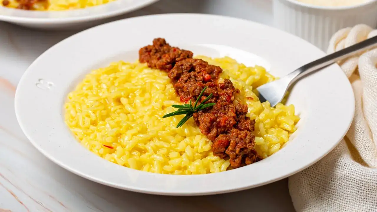 Un cremoso risotto salsiccia e zafferano, guarnito con un ragù saporito e un rametto di rosmarino.