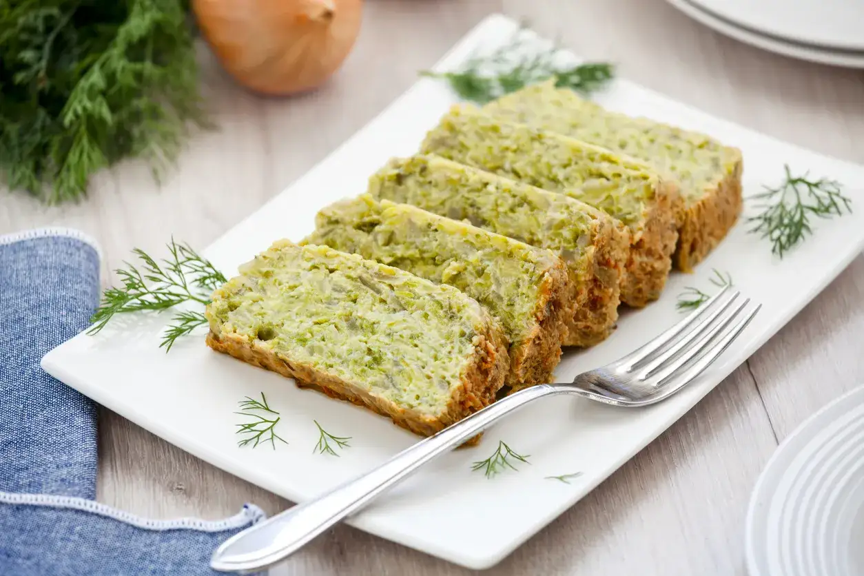 Saporito sformato di zucchine affettato su un piatto bianco, guarnito con aneto fresco.