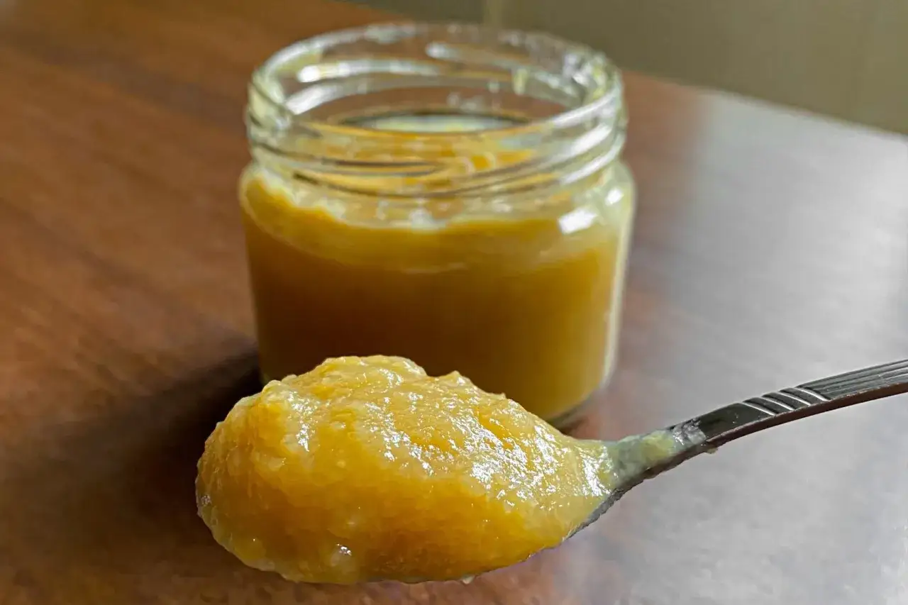 Un cucchiaio pieno di marmellata di mele fatta in casa, con un vasetto sullo sfondo.